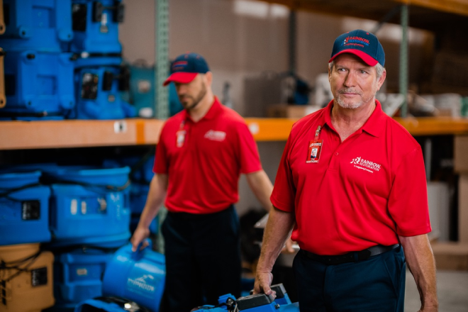 Two Rainbow Restoration service professionals carrying equipment.