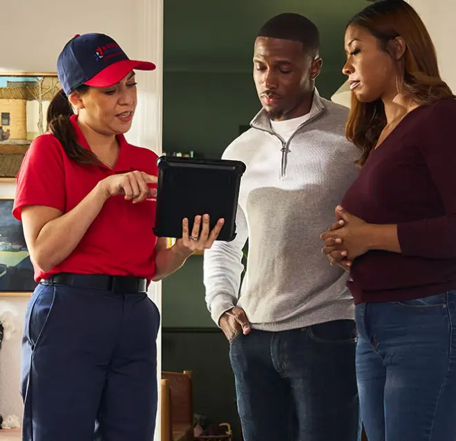 A Rainbow Restoration service professional holding a tablet and pointing out information on the screen to a concerned couple standing next to her.