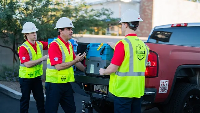 Rainbow Restoration service professionals in hi-vis vests and hard hats unloading restoration equipment from a truck.