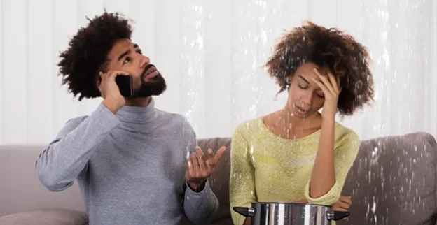 A couple in their Spartanburg, SC, home call a water damage restoration company as water falls from the ceiling and they attempt to catch the water with a large pot.