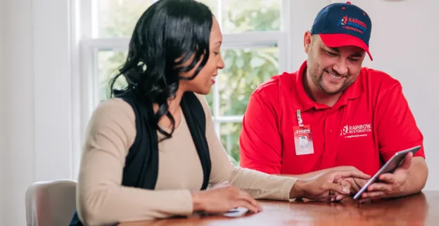 A Rainbow Restoration service professional and a customer sitting at a kitchen table and looking at a tablet.