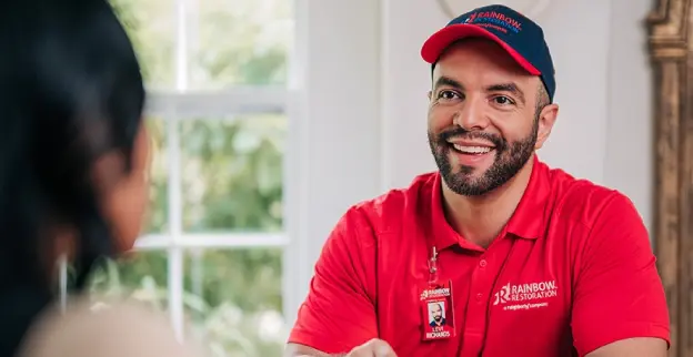 A Rainbow Restoration service professional holds a tablet and discusses property restoration services with a homeowner.
