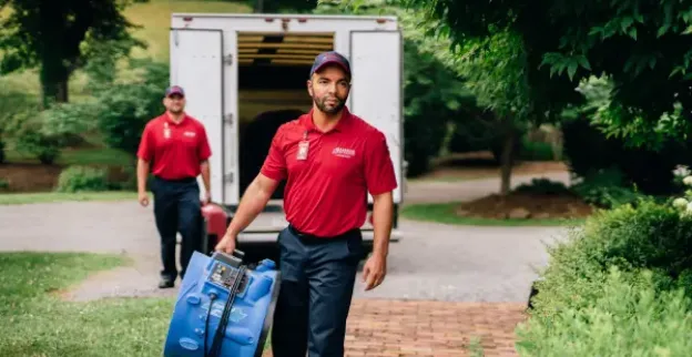 Two Rainbow Restoration service professionals carrying fans from a truck up to a customer's home.