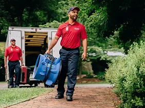 Two members of the Rainbow Restoration team arrive at a property carrying large industrial-sized fans and other equipment.