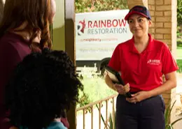 A Rainbow Restoration service professional standing at a customer's door and smiling, having just arrived for water damage restoration.