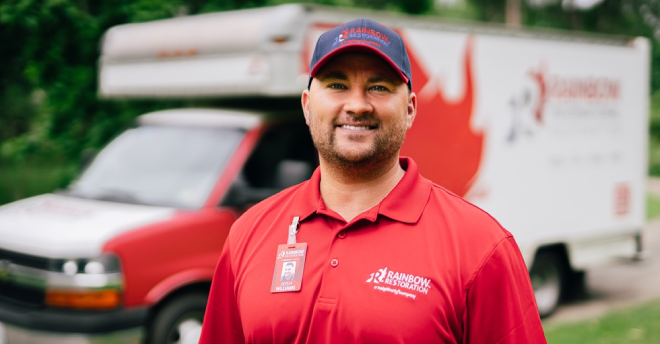 Rainbow Restoration professional stands in front of a branded vehicle.