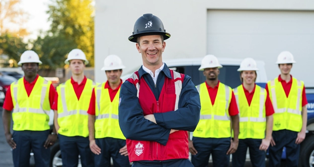 A foreman in safety gear stands smiling in front of a line of Rainbow crew members in safety gear.