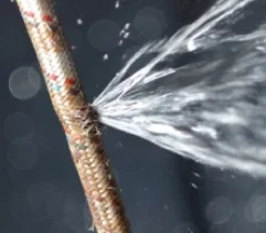 Damaged plumbing hose with water spurting out.