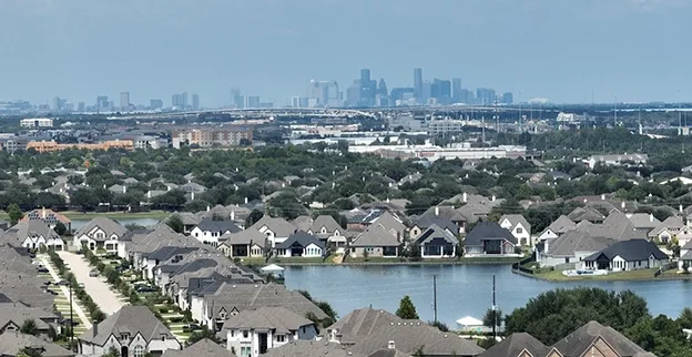 Aerial view of a residential neighborhood in Manvel, TX, with downtown Houston visible in the distance.
