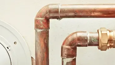 Two copper pipes against a white wall.