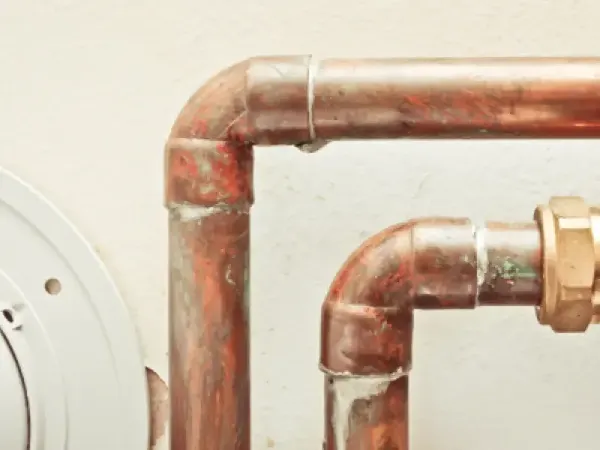 Two copper pipes against a white wall.