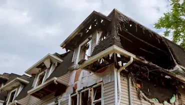 Fire-damaged home with heavy smoke and structural damage to the roof and upper floors after a house fire.