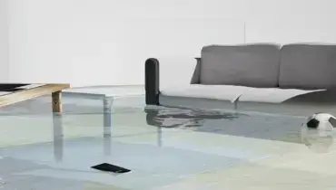 Floodwater covering the floor of a living room near a sofa illustrates how hidden water damage can spread through a home after a leak.