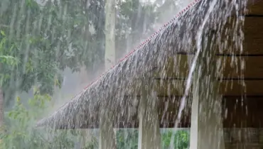 Heavy rain pouring off a residential roof during a storm, illustrating how excess water can lead to potential property damage in Jonesborough homes.
