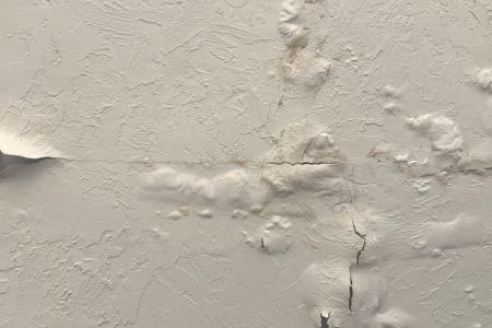 Close-up of a damaged interior wall with bubbling, peeling paint and visible cracks, indicating water damage and moisture trapped beneath the surface.