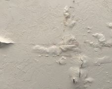 Close-up of a damaged interior wall with bubbling, peeling paint and visible cracks, indicating water damage and moisture trapped beneath the surface.