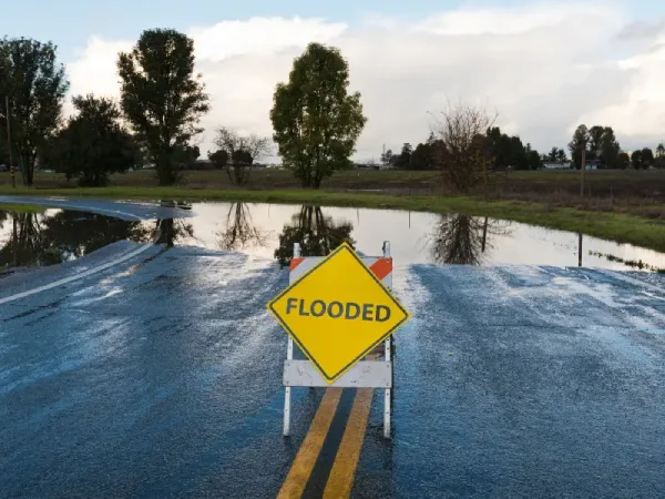 A flooded roadway with standing water and a warning sign illustrates the type of water damage Johnson City homeowners and businesses may face after heavy rain or plumbing failures.