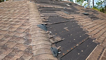 Wind-damaged roof in Johnson City with missing shingles and exposed underlayment, showing how storm-driven rain can enter through roofline vulnerabilities.
