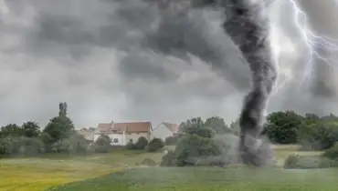 Black tornado funnel cloud and lightning touching down over an open field during a thunderstorm
