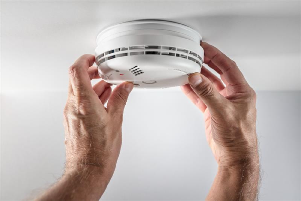 Hands adjusting a smoke detector that is placed on the ceiling.