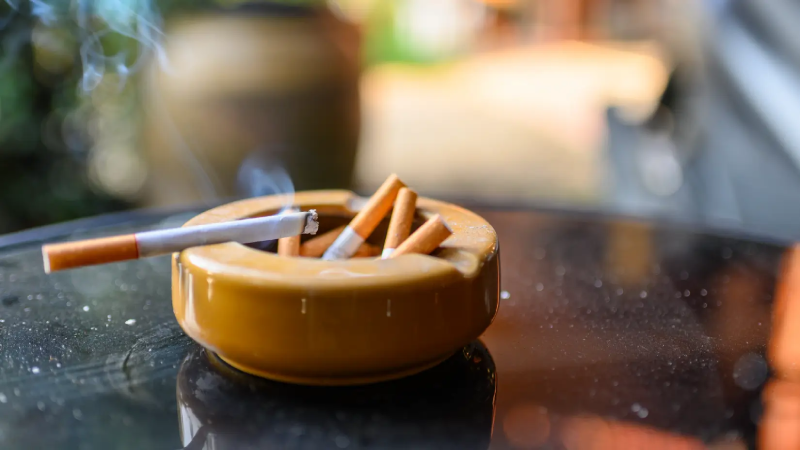 Lit cigarette resting on a yellow ashtray.